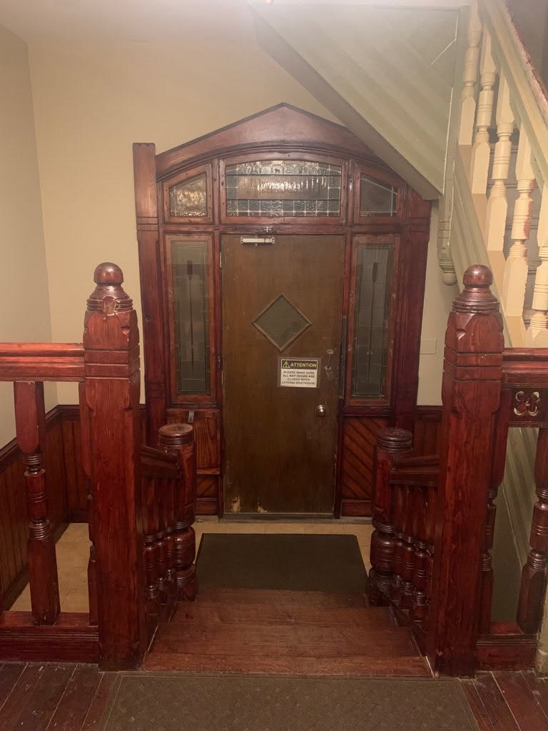 The entrance hall at Crescent Boat Club with decades of paint stripped from the newel posts, balustrade, and door surround, exposing the original wood